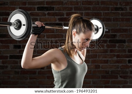Portrait of Attractive fit woman lifting dumbbells on brick background