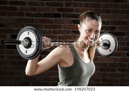Smiling Sweat beautiful girl lifting dumbbells on brick background