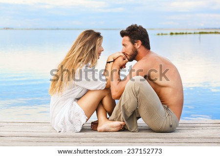 Romantic couple sitting on a jetty under a blue sky at a sunset