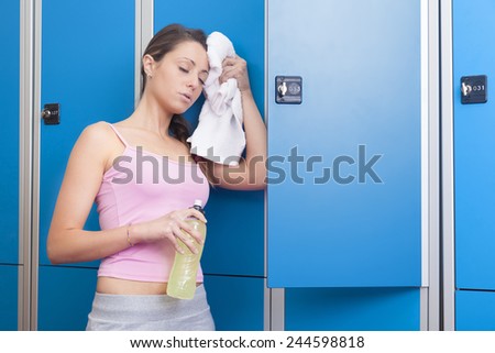 Fitness young beautiful smiling woman with towel and bottle resting in blue dressing room