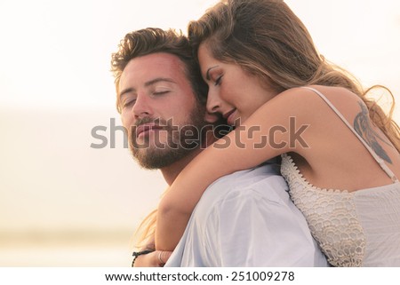 Portrait of a woman embracing her man from behind on sunset background