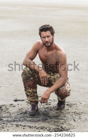 Muscled Shirtless Soldier in Camouflage Pants and Black Shoes on the Beach Sand