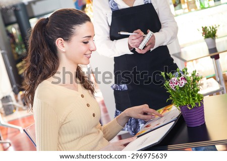 Portrait of young and smiling beautiful woman ordering to a waitress in a restaurant