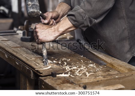Carpenter with a hammer and chisel on the wooden workbench in carpentry