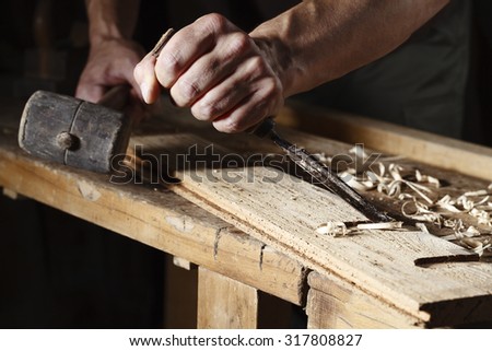 Closeup of a carpenter hands working with a chisel and hammer on wooden workbench