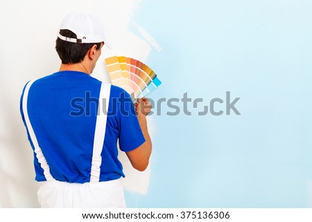 rear view of painter man looking a color palette on half painted wall, with copy space