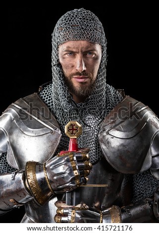 Portrait of Medieval Dirty Face Warrior with chain mail armour and Sword in hands. Black Background