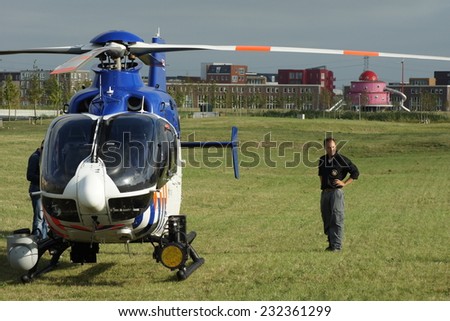 ALMERE POORT, FLEVOLAND, THE NETHERLANDS - SEPTEMBER 2, 2013: Dutch police helicopter stands on grass in a urban park with a police investigator standing standing beside the law enforcement aircraft.