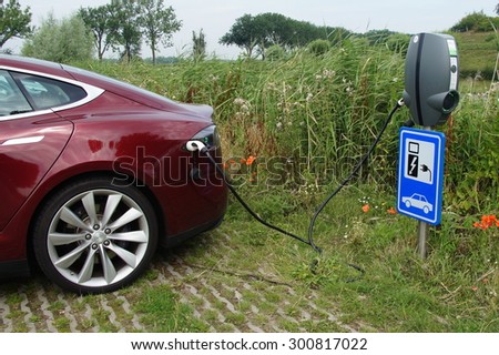 Herwijnen, The Netherlands - July 24, 2015: Electric charging point at a public car park in Herwijnen. The charging station is on the right with the Tesla Model S is plugged in with a cable.