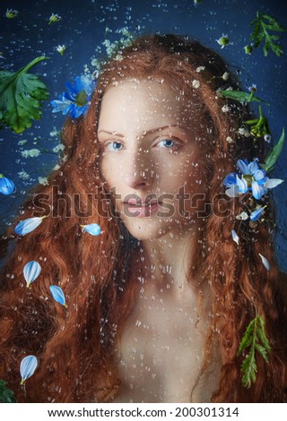 Beautiful Red haired Young Woman behind the Window with Water Drops on it and flowers