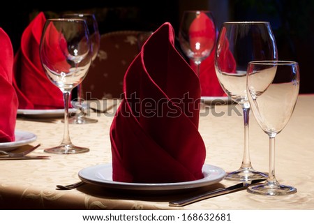 Table In A Restaurant With A Yellow Tablecloth, Red Napkins, Wine Glasses And Cutlery.