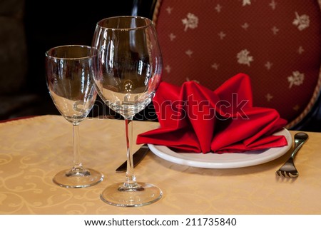 Hotel service: table in a restaurant with a white tablecloth, red napkins, wine glasses and cutlery.