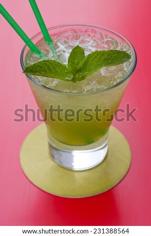 A glass of mint lemonade. Red background. Up view.