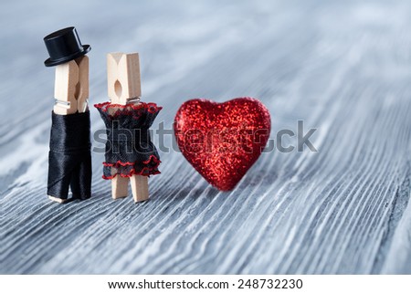 Romantic couple. Wedding invitation. Valentines day. Man, woman and read heart. Groom in black suit hat and bride in black dress. Clothespins. (Soft focus)