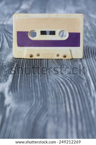 Music template postcard. Violet audio cassette on the gray wooden background. Vintage, retro style. Soft focus.