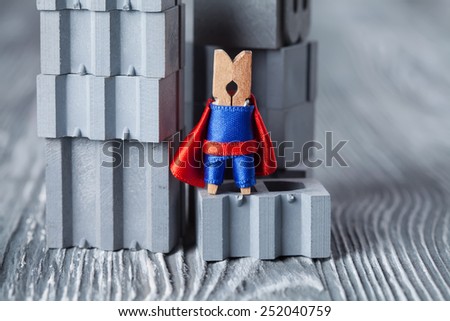 Clothespin superhero in blue suit and red cape. Gray background, building blocks, construction. Confident clothespin. (retro style, soft focus).