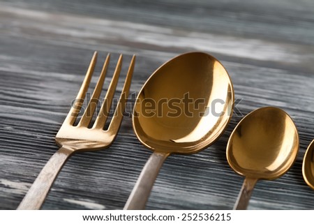 Tableware set (gold spoons and fork)  on the gray wood background. scratches and scrapes. Soft focus.