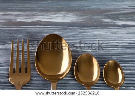 Tableware set (golden spoons and fork)  on the gray wood background. scratches and scrapes. Soft focus.