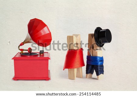 Vintage red color gramophone. Retro plastic toy. Clothespins: romantic couple. Man, woman. Gentleman in black hat and woman in red dress. (Old paper background and texture)