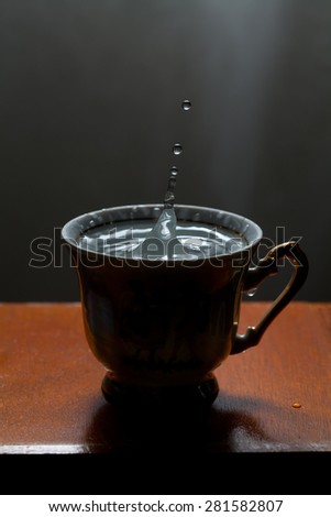 Blue water drops, splashing in the vintage cup. Classic wooden table. Frozen motion. soft focus, macro view