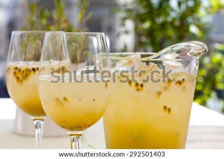 Fresh, cold, yellow drink in glass jug and wine glasses. Maracuja, kiwi lemonade pitcher on the white table. Summer, daylight, closeup. Side view. Soft focus