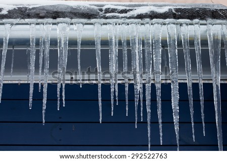 Cold weather concept. Icicles on the roof. Winter season. downspout. Blue wooden background. Cold time. Day. Soft focus