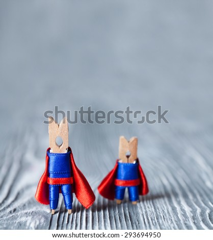 Leadership concept. Clothespins superheroes in blue suit and red cape. Big and small superman.  Gray wood abstract design background. soft focus.