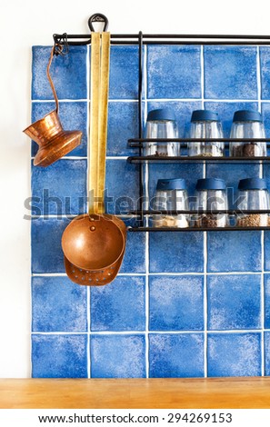 Metal shelf with different seasonings, spices in glass bottles.\
Vintage copper spoon, skimmer, coffee maker, turk. blue tile wall and wood table background. Kitchen utensils retro design. Copy space.