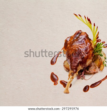 Well-browned and crisp duck confit.  French dish made with the leg of the duck. Roasted duck leg with potatoes and brown garlic bacon sauce, seasoned herbs. Aged paper background. Copy space.