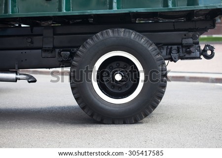 Retro lorry truck. Green color, down side. Body, silver exhaust pipe, car wheel, asphalt background. Macro view. soft focus.