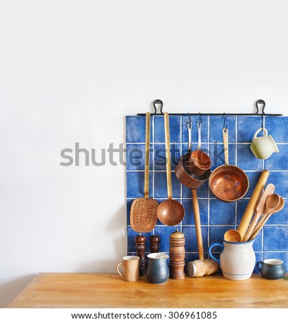 Kitchen interior, accessories. Hanging copper kitchenware set. Spoon, skimmer, colander. Blue tiles ceramic background. Wooden spoons, pitchers and cup on the table. copy space.