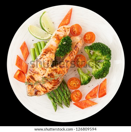 Salmon steak in plate with vegetables isolated on black background