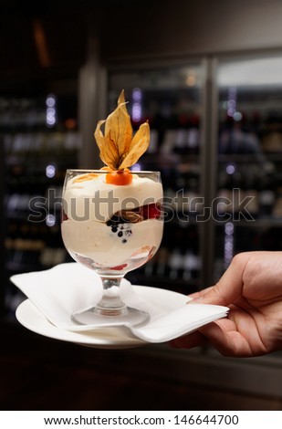 Waiter offering dessert, wine cabinet in background