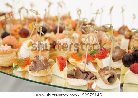 Small fish, meat and cheese snacks in plate on banquet table close-up