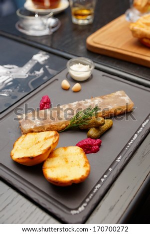 Meat aspic with baked potatoes, gherkins and horseradish on stone plate