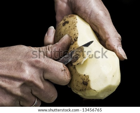 Man\'s hands peeling potato with serrated knife fading into black background. Shot with macro lens, very detailed image