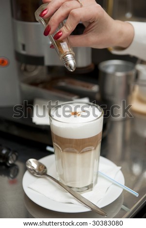 Barista decorating latte drink with cocoa powder, shallow depth of field