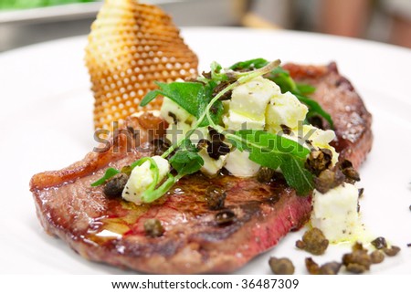 Rare cooked steak with capers, potato chip and cheese topping