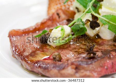 Rare cooked steak with capers and cheese topping, close-up