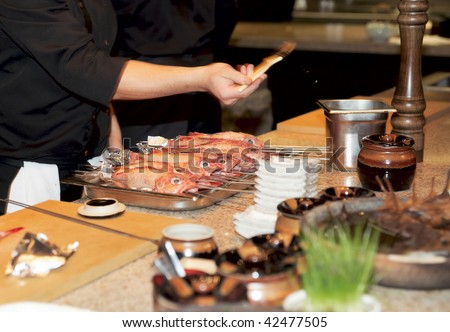 Chef prepares fish for grill - adds oil and seasoning with brush, motion blur on hand