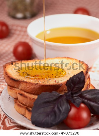 Three pieces of toasted bread and cherry tomatos, oil being poured on bread