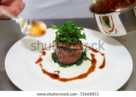 Chef is decorating tenderloin steak with sauce, motion blur on spoon