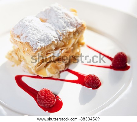 Slice of mille-feuille cake with raspberries and sweet sauce on porcelain plate
