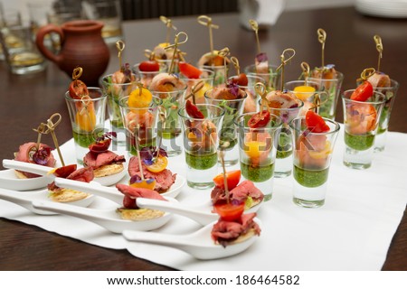 Various meat and seafood snacks in shot glasses on table