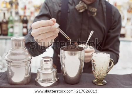 Bartender is making cocktail at bar counter, adding some bitter in the shaker, toned image