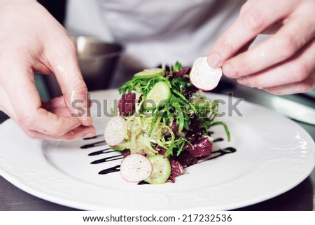 Chef is decorating appetizer with lettuce mix, toned image