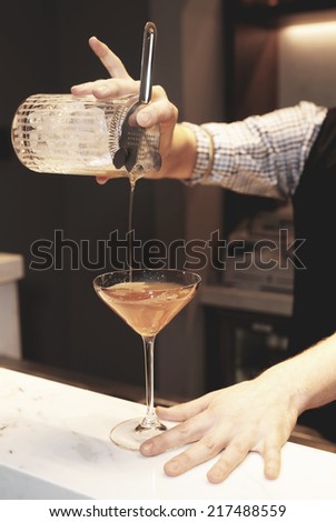 Bartender is making cocktail at bar counter, toned image
