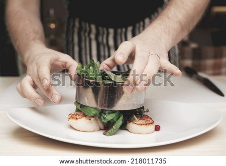 Chef is cooking appetizer with sea scallops and salad mix, toned image