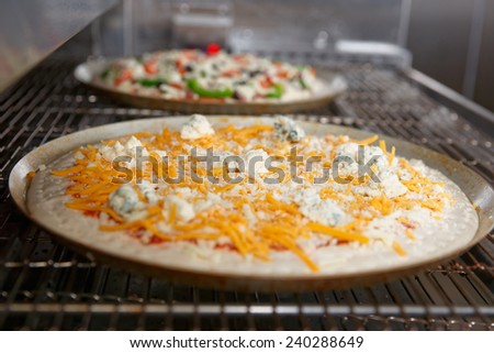 Cheese pizzas entering the industrial oven, close-up