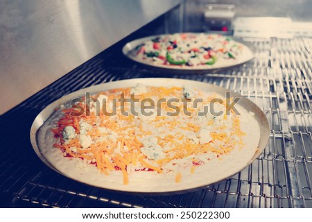 Cheese and vegetable  pizzas are entering the industrial oven, toned photo